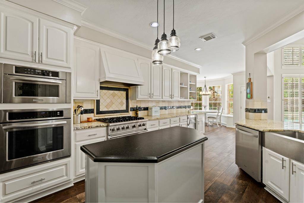 This kitchen features modern stainless steel appliances, white cabinetry, and a central island with solid surface countertop. It has a cozy breakfast nook with large windows and tile wood like flooring, offering a bright, inviting space for cooking and dining.