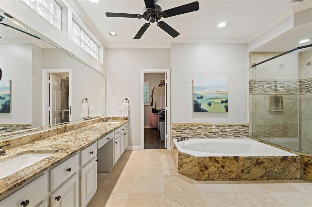 This spacious bathroom features a double vanity with granite countertops, a large mirror, and ample cabinet space. It includes a walk-in shower and a luxurious soaking tub. High ceilings, recessed lighting add a modern touch.
