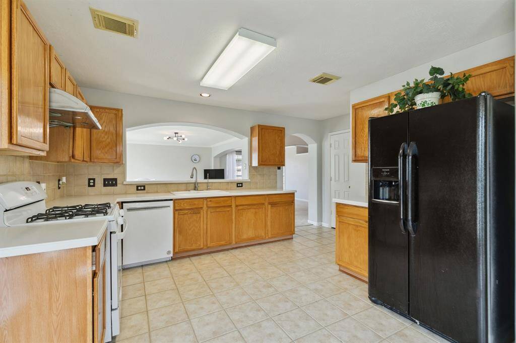 This light-filled kitchen exudes warmth and functionality, featuring classic tile flooring, rich wooden cabinetry, and a gas stove. Expansive windows and a glass door open to the patio, seamlessly blending indoor and outdoor living while enhancing the kitchen’s bright, airy ambiance