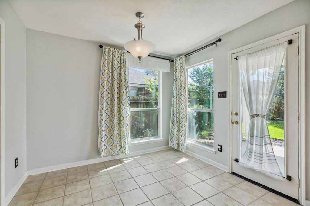 This breakfast area is adorned with large windows dressed in tasteful patterned curtains, complemented by a glass door that opens to the backyard. Sleek tile flooring and a contemporary light fixture enhance the space, creating a warm and inviting ambiance perfect for everyday meals or entertaining guests.