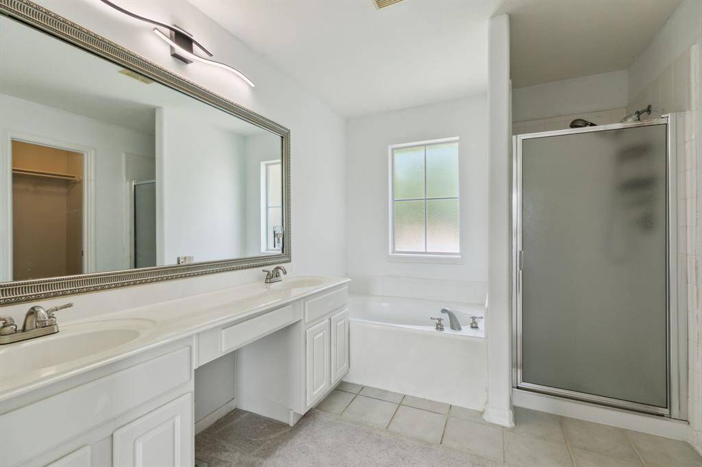 This bathroom features a spacious layout with a dual sink vanity, large mirror, and modern lighting. It includes a separate shower and a soaking tub beneath a frosted window, offering both style and functionality.