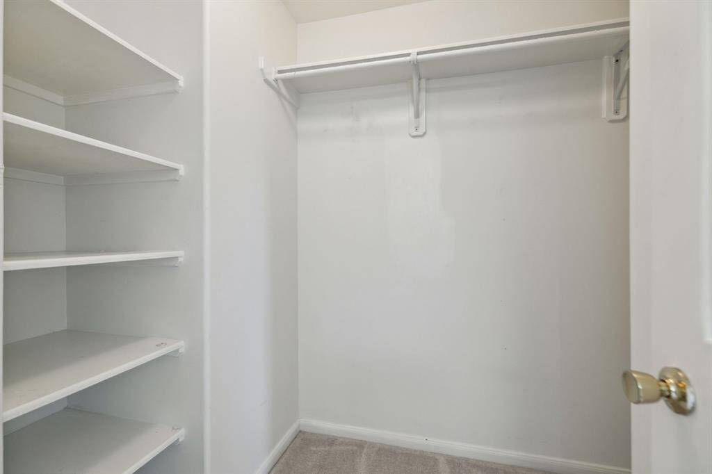 A clean, empty walk-in closet featuring crisp white walls, built-in shelves on the left, and a hanging rod on the right—designed for optimal organization and storage