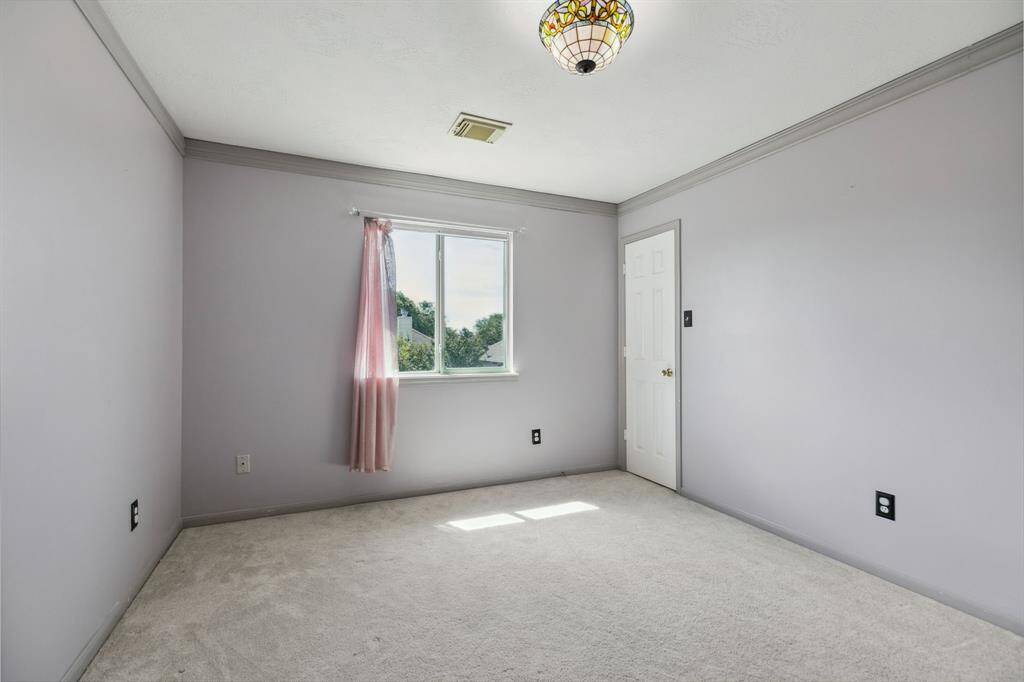 This room features ample natural light from a large window, a ceiling fan, and neutral carpeting, creating a bright and airy space.