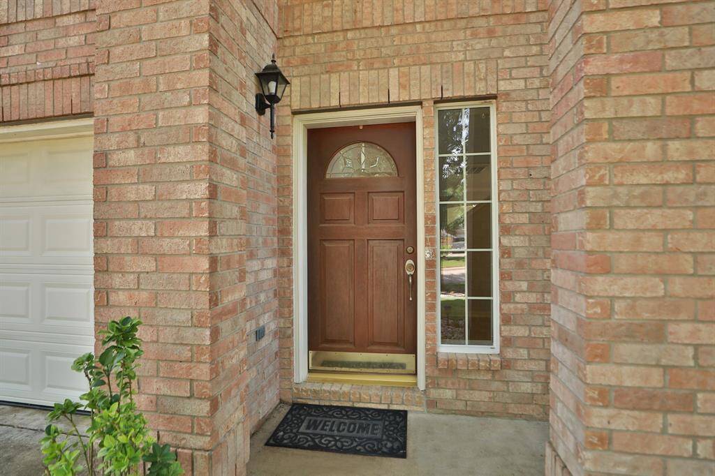 The porch showcases a welcoming entryway with a solid wooden front door, flanked by a tall window, set against a brick exterior.