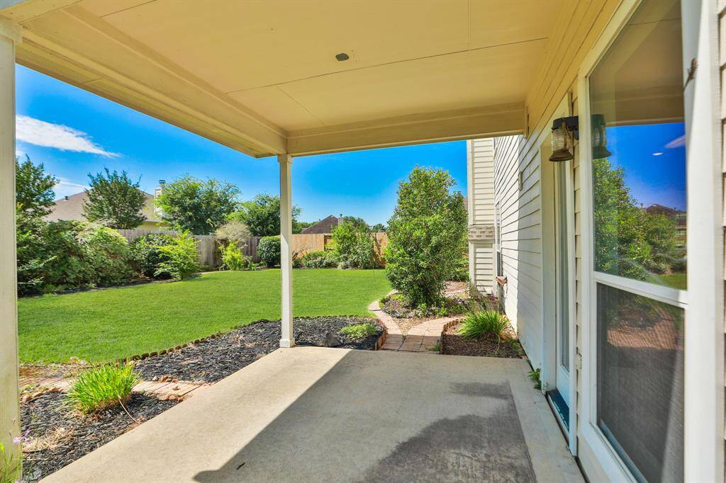 A covered patio overlooking a spacious, landscaped backyard adorned with lush greenery and set beneath a clear blue sky—an ideal setting for outdoor relaxation and entertaining.