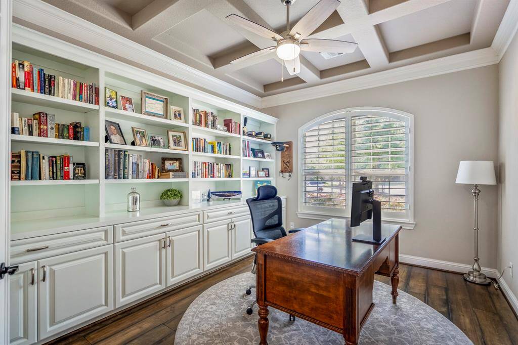 French doors lead into a spectacular study offer a wall of custom built-ins, an arched window with plantation shutters, and blocked coffered ceiling.
