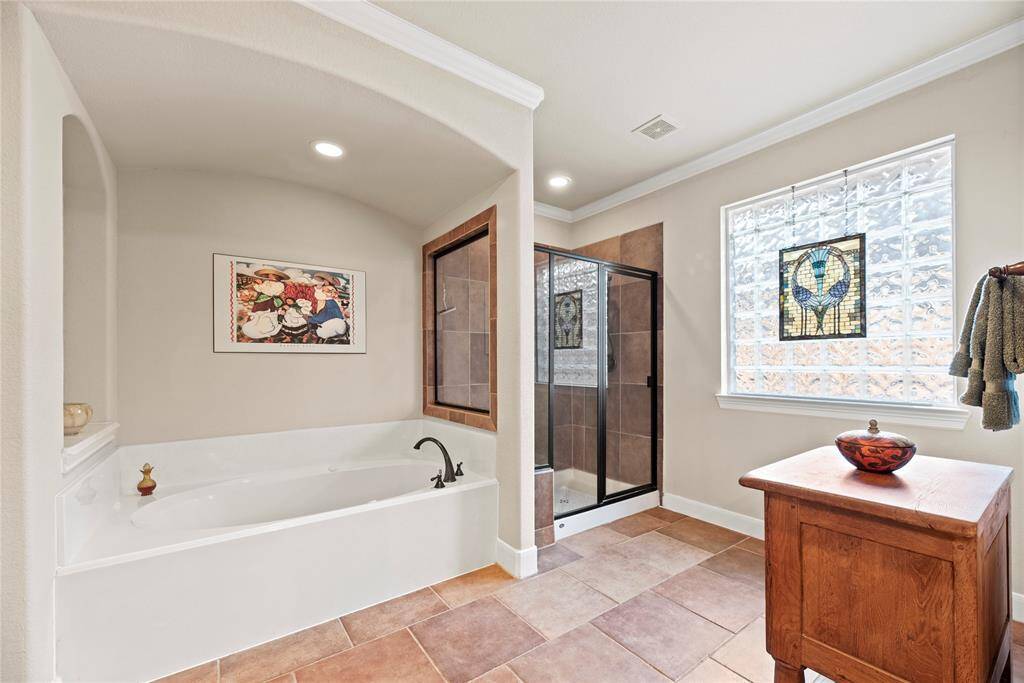 This ensuite also offers an oversized soaking tub and a separate walk-in shower with a glass door, large window, and gorgeous tile work.