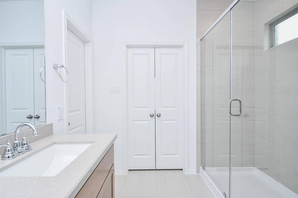 The double doors, center, open onto the primary bedroom; while the bright, walk-in, glass enclosed shower offers lots of refreshing room. Note the darling window, above.