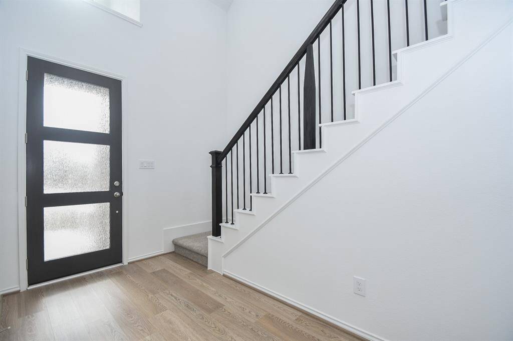 Clean lines complement the contemporary striking black/white theme in this inside view of the front entry; with frosted glass panes on the door, and dark wrought iron balusters on the conveniently placed carpeted stairway.