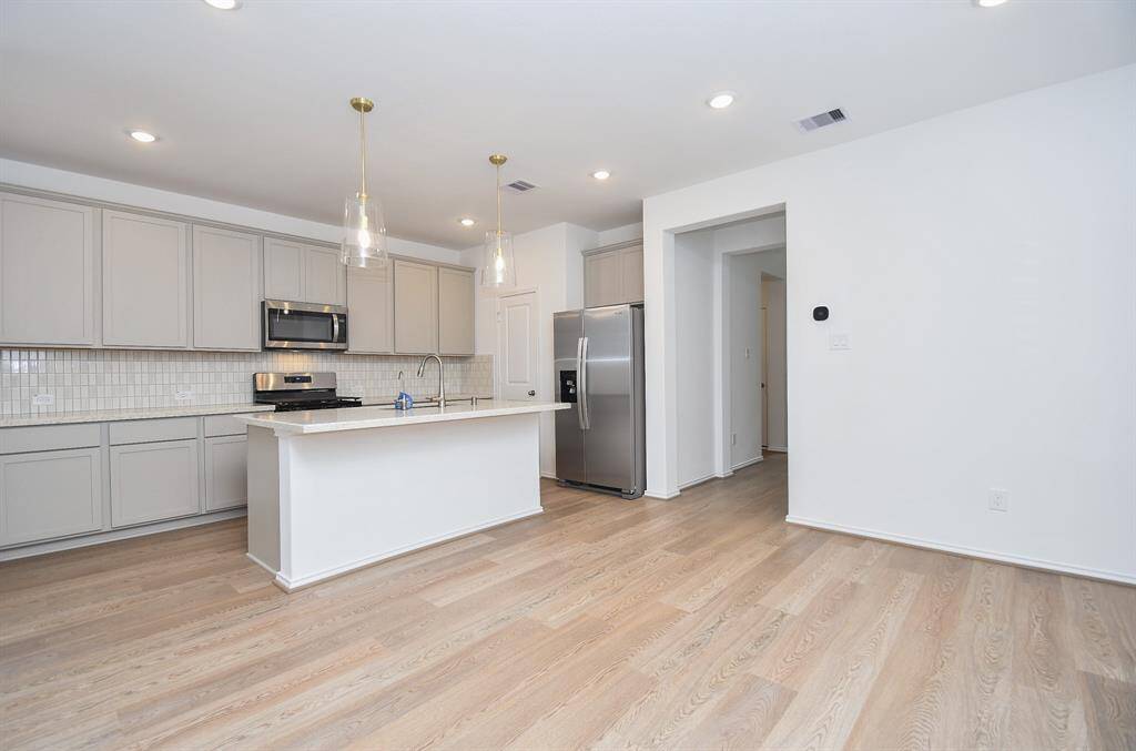 Clear glass pendant lighting beautifully hovers over the island/sink and beautifully extended cream toned granite counter top, perfect for comfy stools, below. The pleasing linear configuration of abundant cabinetry and pale tile backsplash makes for any cook's dream culinary workshop!