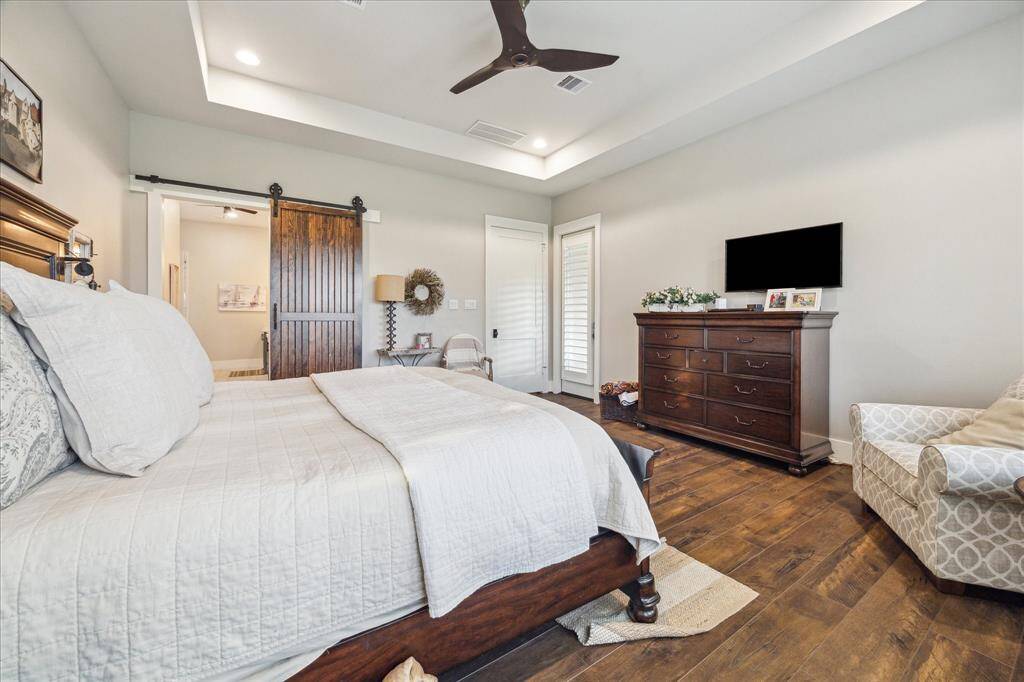Primary suite with tray ceiling, wood floors, and barn door access to the spa-like bathroom retreat.