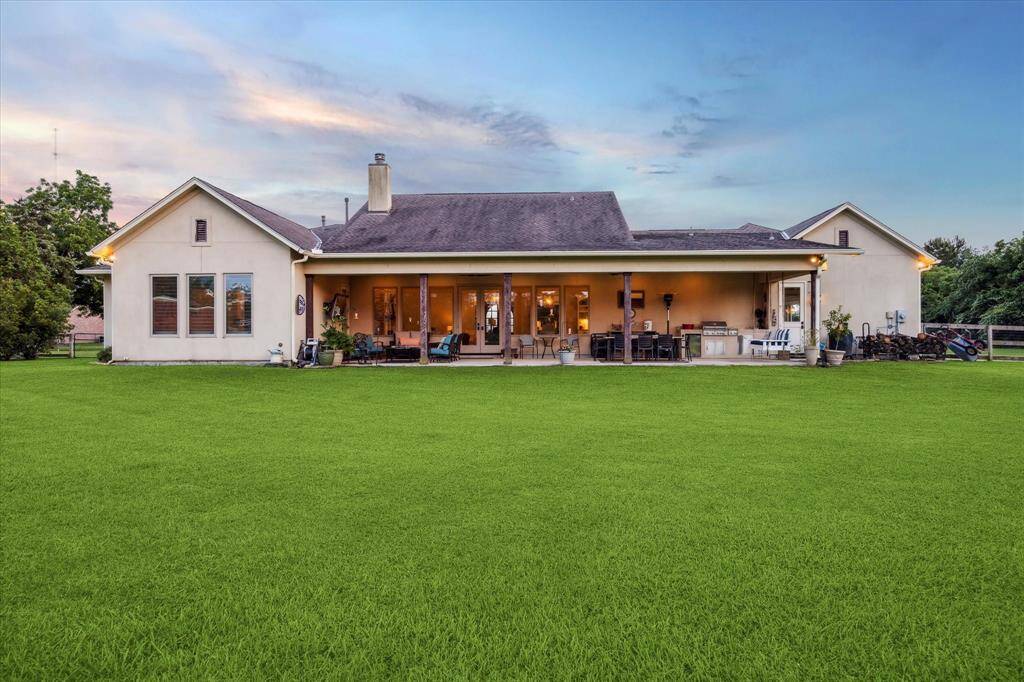 Stunning backyard elevation showcasing the deep covered patio, outdoor kitchen, and glowing interior windows.