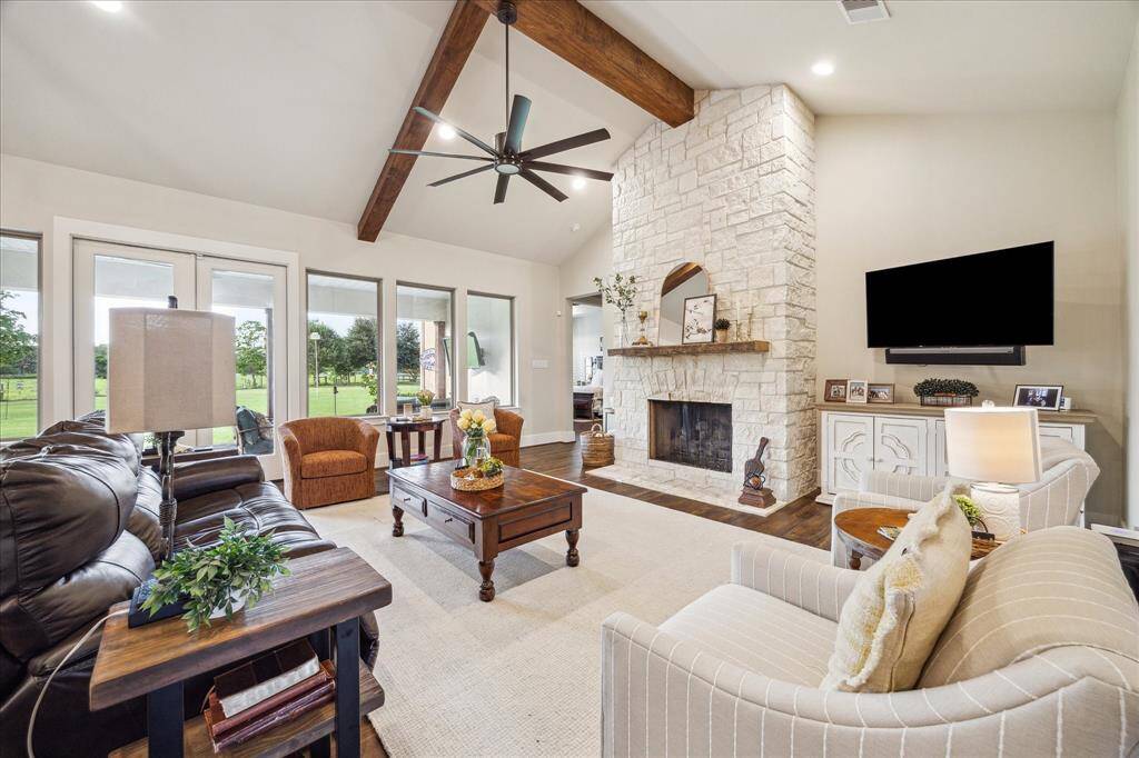 Stone fireplace anchors the living room with timeless texture, framed by backyard views and warm wood flooring.