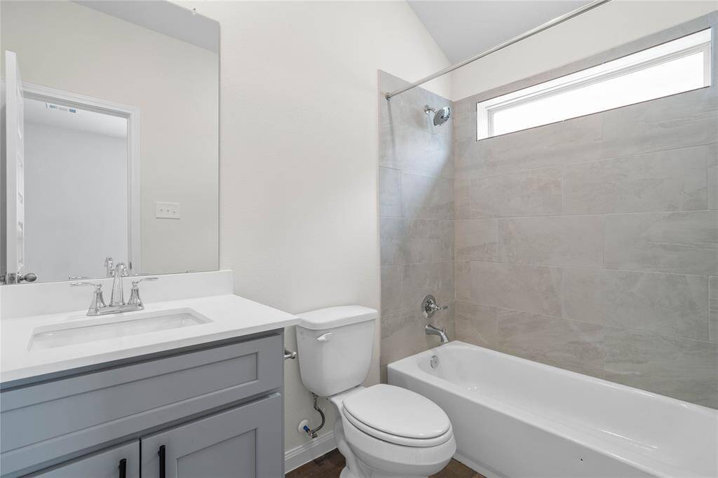 Secondary bath features tile flooring, bath/shower combo with tile surround, stained wood cabinets, beautiful light countertops, mirror, sleek fixtures and modern finishes.