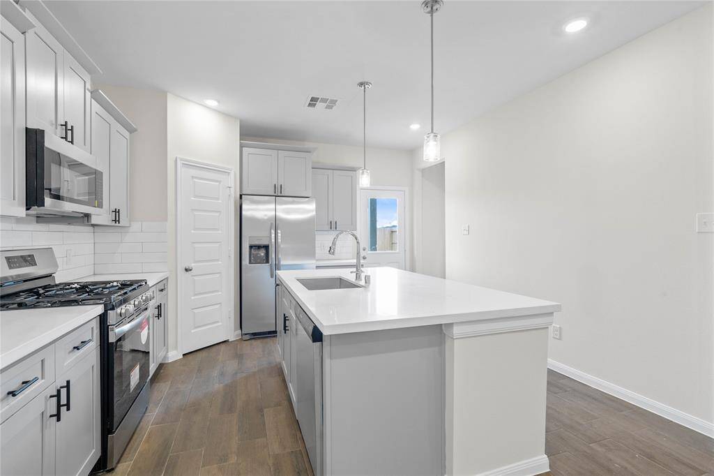 The kitchen features stained cabinets, stainless steel appliances including microwave, refrigerator, gas range, and dishwasher, modern tile backsplash, silestone quartz countertops, recessed and pendant lighting, stainless steel single sink and tile flooring!