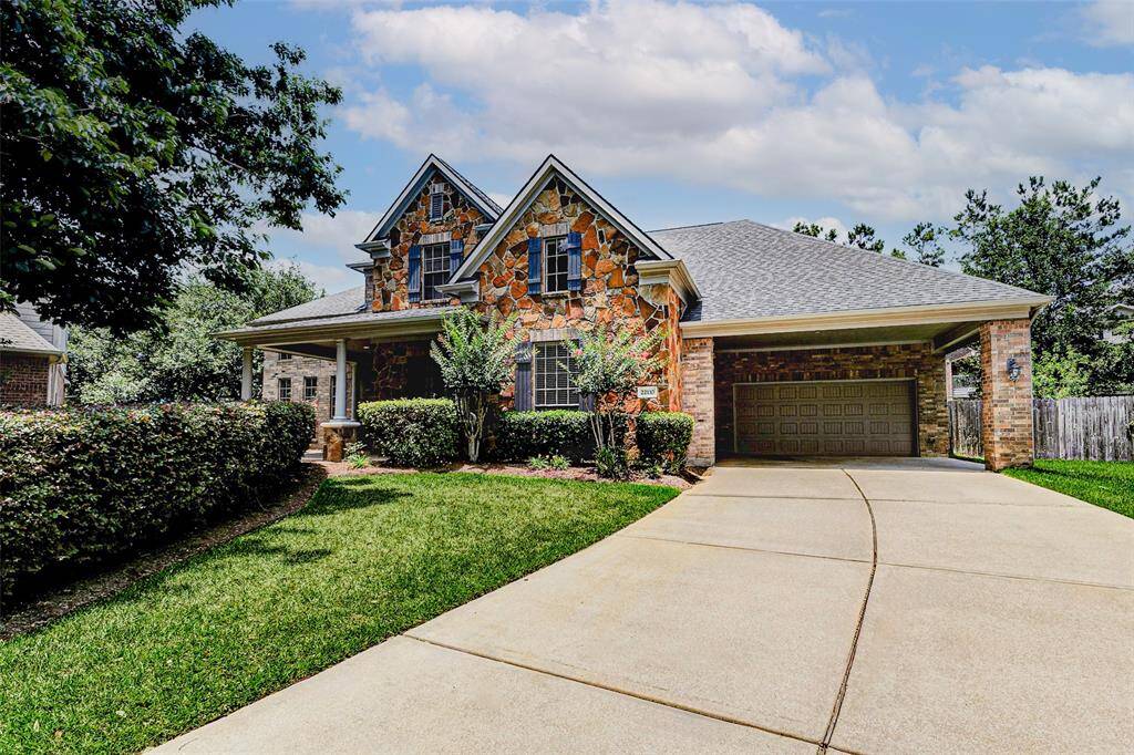 This home features a charming stone facade with a welcoming front porch, a spacious driveway leading to a 3-car garage.