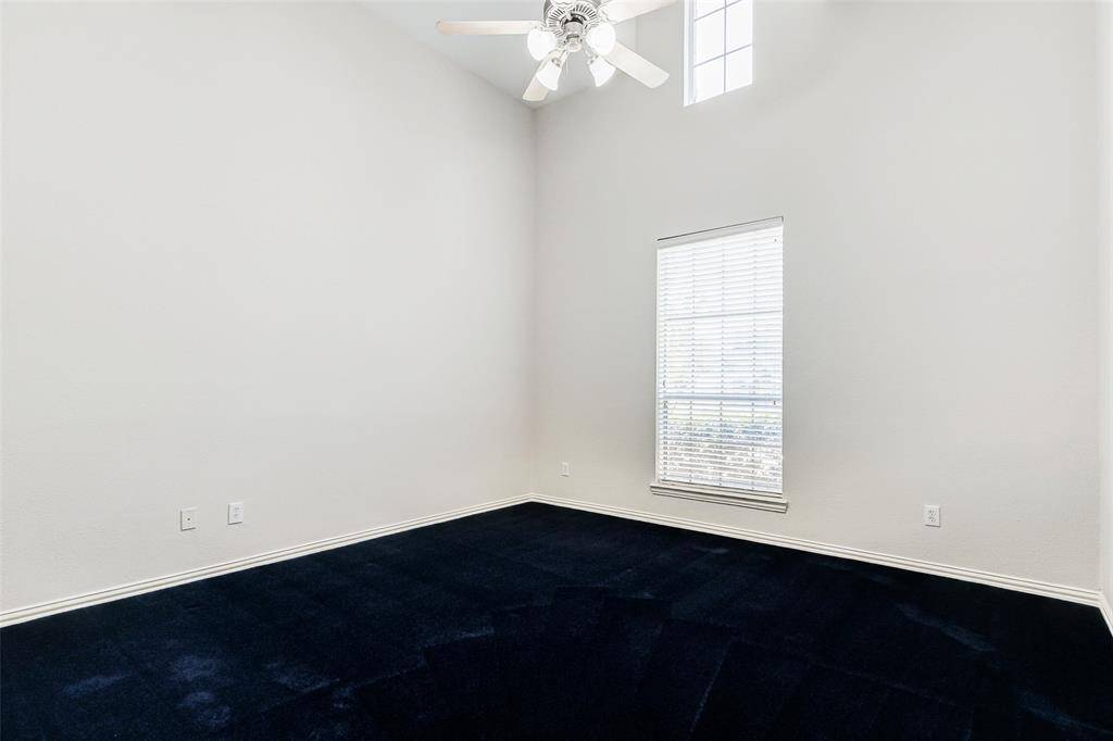The second bedroom down features high ceilings, a ceiling fan, and a large window for natural light. It has neutral walls, creating a spacious and airy feel.