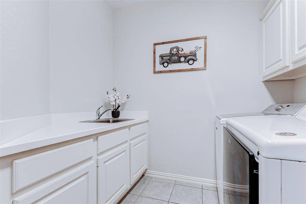 The laundry room is bright with white cabinetry, and a countertop with a sink. The space offers a functional and organized area for laundry tasks.