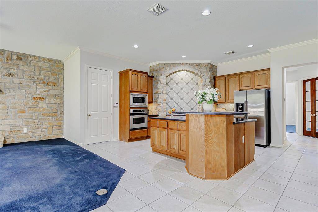 Another view of the spacious kitchen featuring a central island with a stone accent wall, and modern stainless steel appliances. The adjoining area has a stylish stone wall, creating a blend of comfort and elegance. The insulated door next to the ovens leads to the 3-car tandem garage.