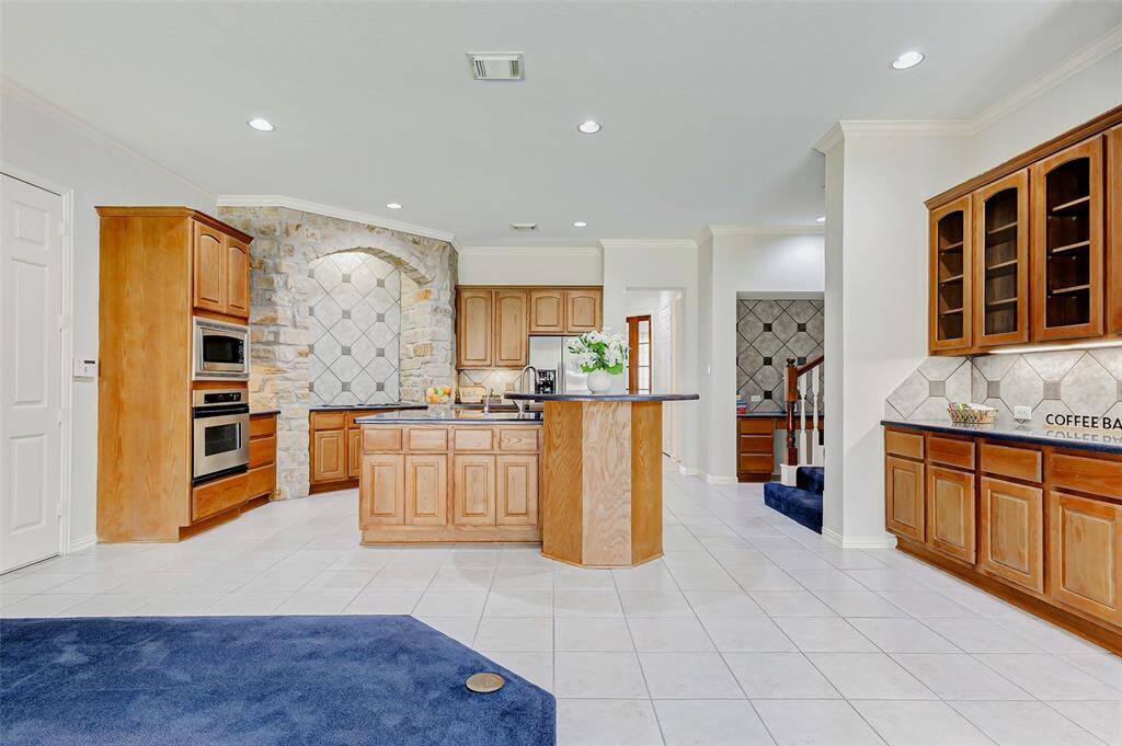 This view of the kitchen features a stone accent wall surrounding the 4 burner cooktop which adds a touch of elegance. There are glass inserts on the upper cabinets to the left with more countertop space. in the background near the stairs is another countertop & cabinets providing flexibility and convenience to the kitchen area.