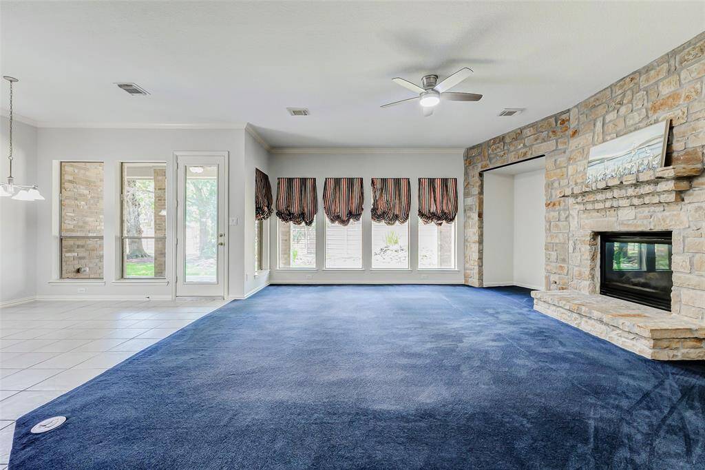 The spacious living area features a cozy stone fireplace, large windows with natural light, and a ceiling fan. The room opens to a tiled breakfast area with modern lighting.