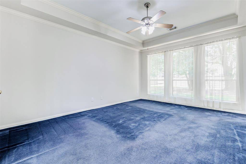 The primary bedroom has large windows providing ample natural light and a ceiling fan providing a view of the large backyard.