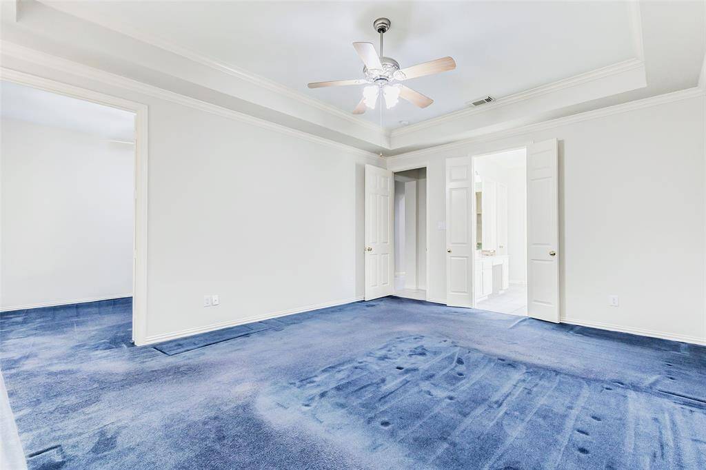 The spacious primary bedroom features a tray ceiling and connects to the primary bathroom through double doors, offering a bright and airy feel. The open area to the left leads to the extra room off the primary. The other door leads out to the living areas on the first floor.