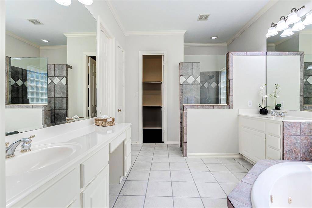 The primary bathroom features dual vanities, a spacious walk-in shower with tile accents, and a large soaking tub. There is a make-up area in the larger vanity area. The neutral palette and ample lighting create a bright and inviting space, complemented by a convenient walk-in closet.