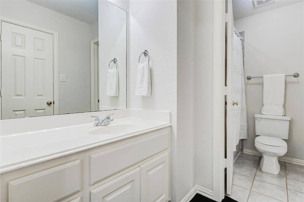 This bathroom is adjacent to the other secondary bedroom. It includes a spacious countertop with a single sink, a large mirror, and a separate area with a shower that connects to the other secondary bedroom/bathroom vanity area.