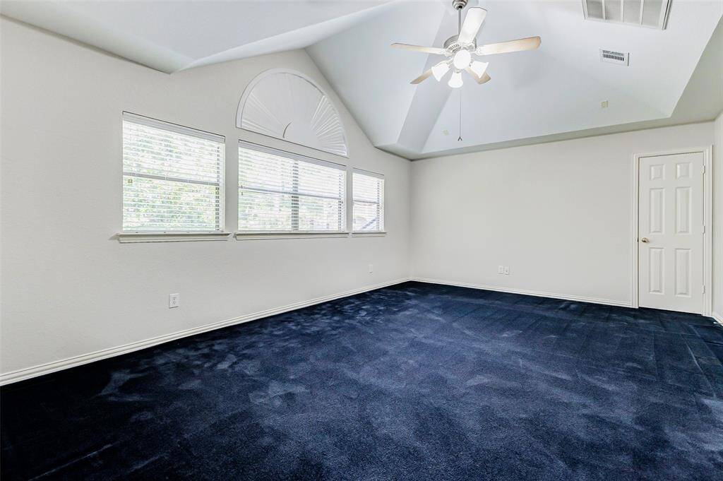 This spacious game room features a vaulted ceiling with a fan and large windows for natural light. The neutral walls provide a blank canvas for personalization. Windows overlook the sizable backyard.