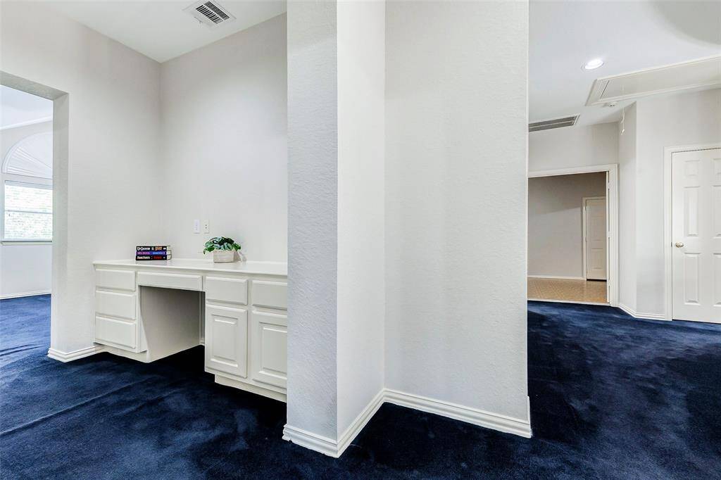 This area features a home office nook or study area with built-in white cabinets and a desk. The space is bright and open, with adjacent rooms visible through doorways, suggesting a versatile layout.