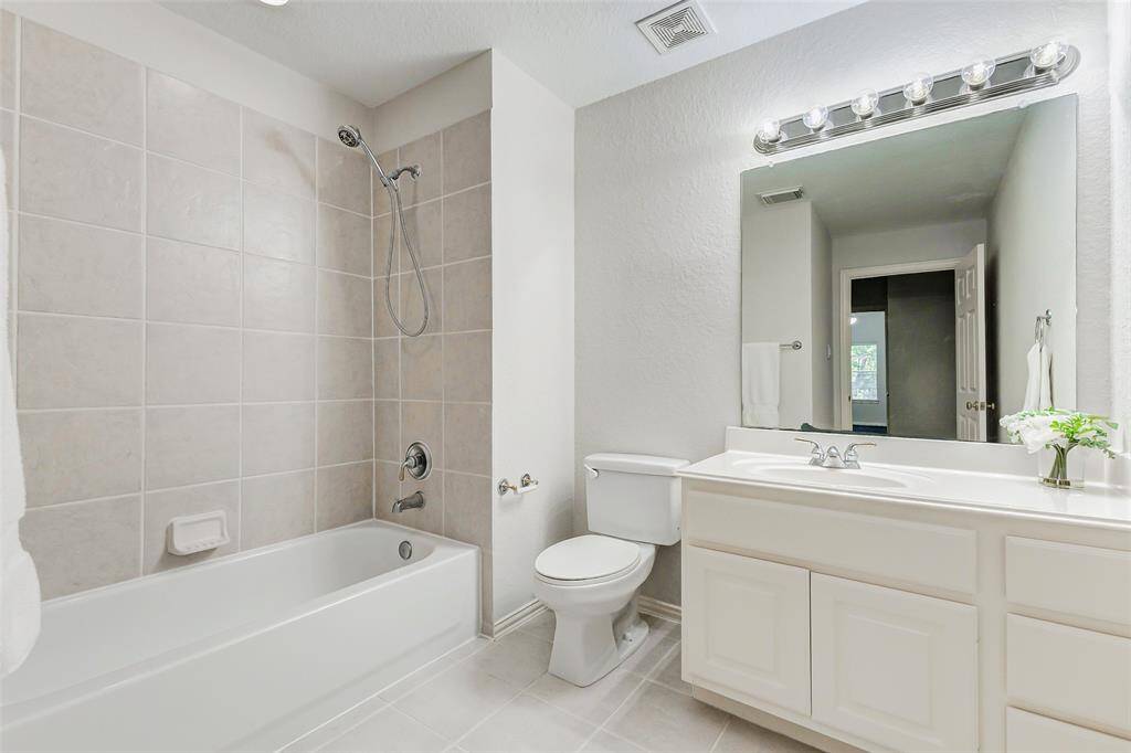 This secondary upstairs bathroom features a clean, modern design with neutral tile work, a combined shower and bathtub, a large mirror with vanity lighting, and a spacious countertop with under-sink storage.