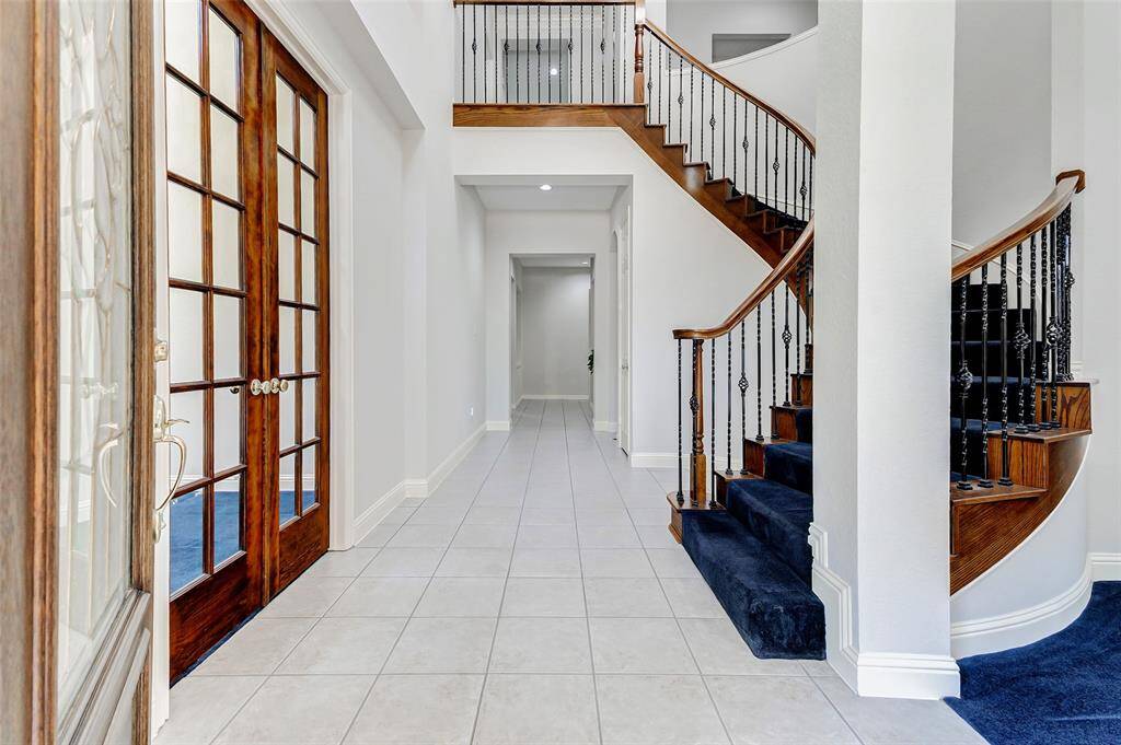 This bright, spacious entryway with elegant wooden double doors, a curved staircase and tile flooring provides a welcoming atmosphere. All the natural light creates an inviting ambiance.