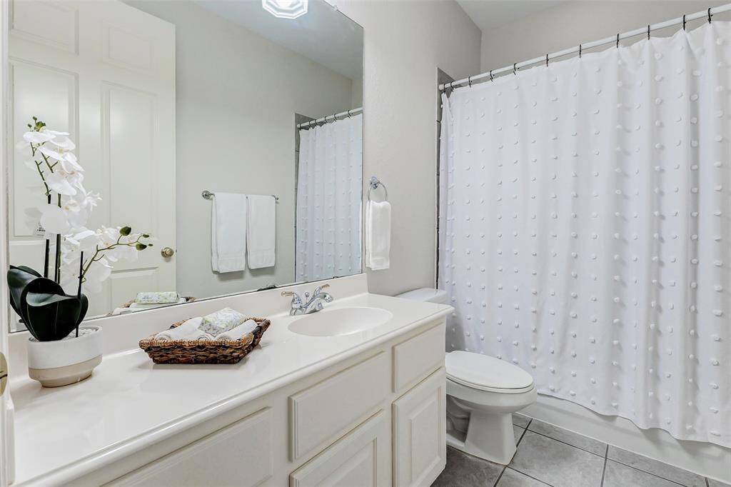 This secondary bathroom on the first floor is adjacent to the secondary 1st floor bedroom. It features a clean, modern design with white cabinetry and countertop. The space is bright and well-maintained, with tiled flooring.
