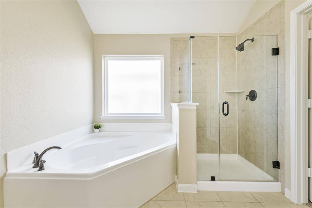 Lots of natural light shines on a large soaking tub and separate frameless shower with upgraded bronze fixtures and hardware.