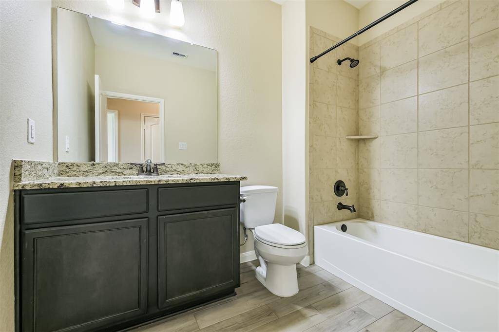 Hall bath with granite counters, wood look floor tile, tub/shower combo with bronze fixtures.