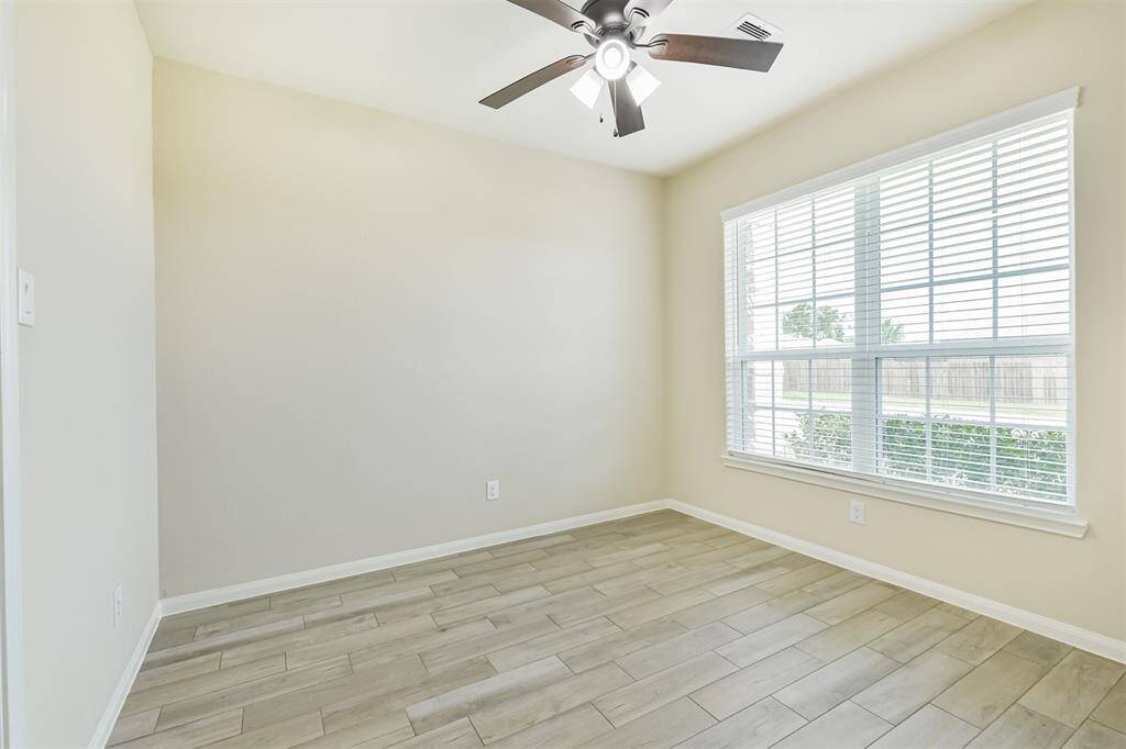 Fourth bedroom used as a study with large window, ceiling fan, and wood look tile.