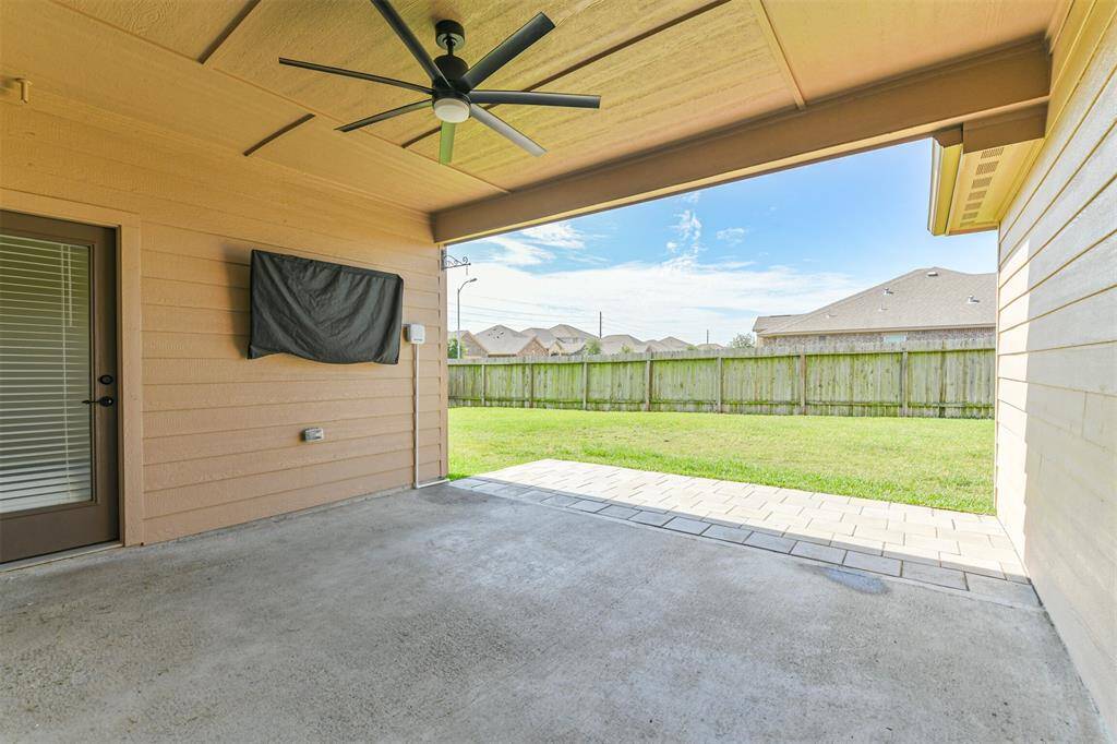 Spacious covered back porch includes remote controlled ceiling fan, mounted TV, sprinkler system controls, and extended patio blocks. Greenspace separates this backyard from houses behind.