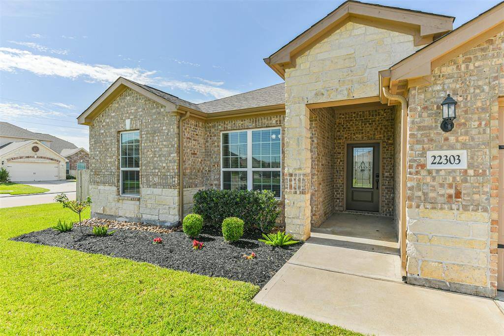 Landscaped beds lead to a covered front porch and a glass and wood front door.