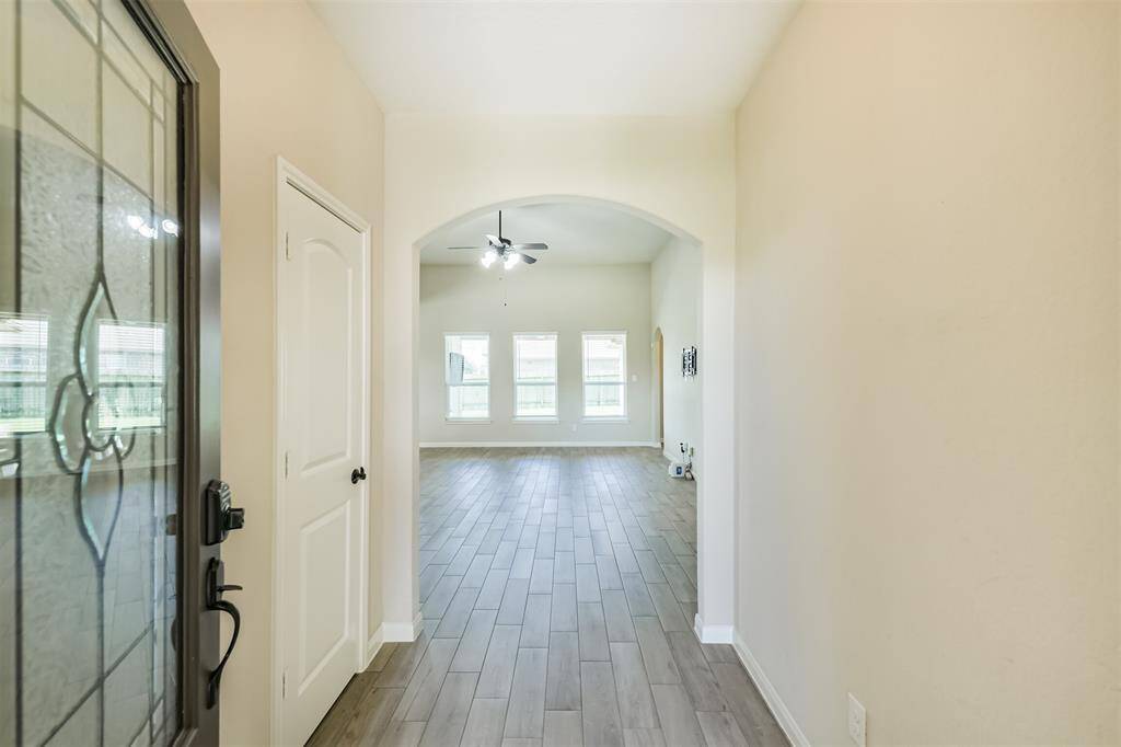 Entry with coat closet leads to large living room with multiple windows, high ceiling, and fan. Wood look tile flows throughout the main living areas.
