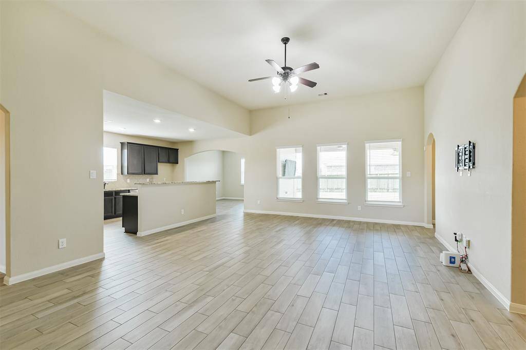 Light and bright living room with high ceiling, ceiling fan, and wood look tile adjoins the spacious kitchen and dining room.