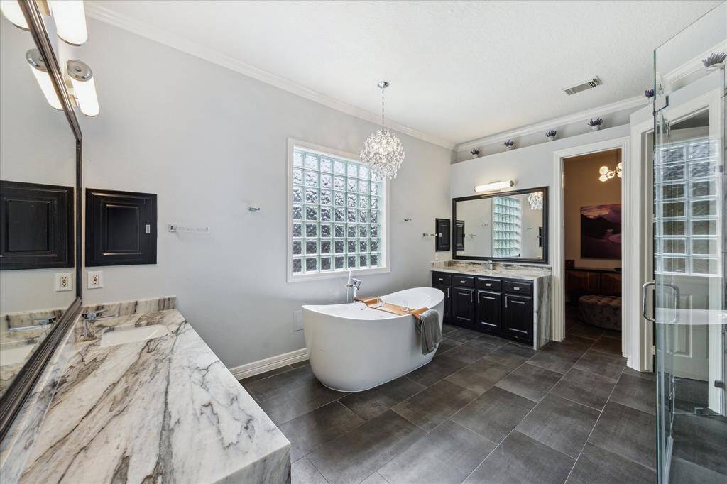 Fully Renovated Spa Bath Retreat: This recently renovated en-suite features on-trend rectangle tile floors, a new modern jetted soaking tub beneath a sparkling chandelier, freshly painted cabinetry, and marble waterfall-edge counters that bring luxury into everyday living.