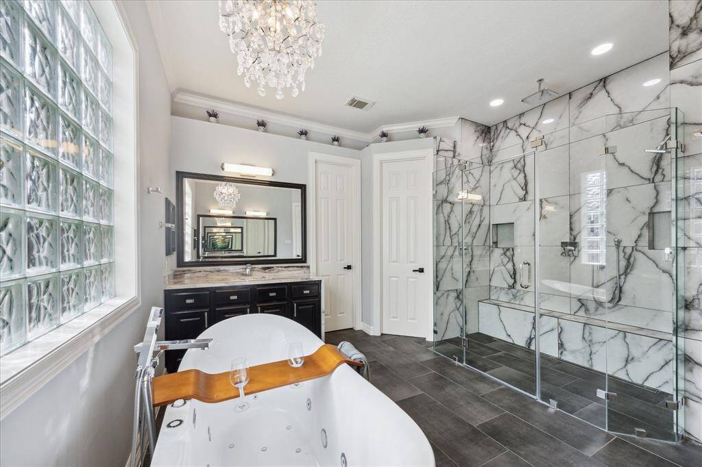Statement Shower with Marble Detail: The oversized walk-in shower was fully redone with dramatic marble-look tile, dual shower heads, a built-in bench, and frameless glass for a spa-inspired experience that feels truly elevated.