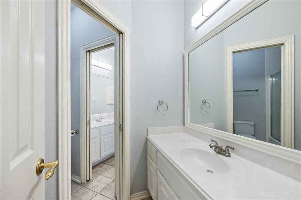 Updated Shared Bath with Private Vanities: Connected by a jack-and-jill layout, this updated bath features painted cabinetry, framed mirrors, and separate vanity access for added privacy.