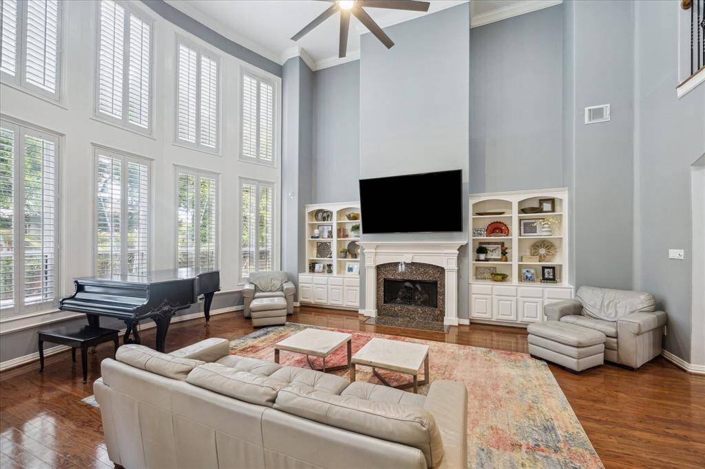 Custom Built-Ins & Elevated Ceilings: The fireplace anchors the room with flanking built-ins with open upper shelving and closed lower cabinets, while two-story ceilings add volume and a sense of openness.
