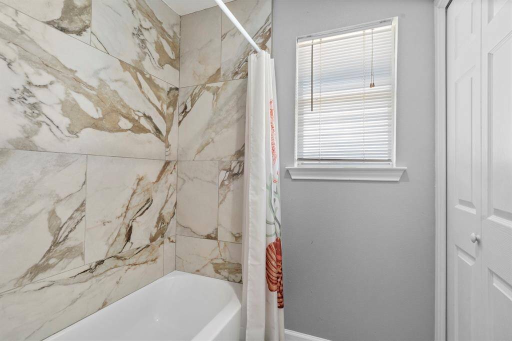 Sleek tub/shower surround with luxurious marble-look tile and a clean, neutral color palette.