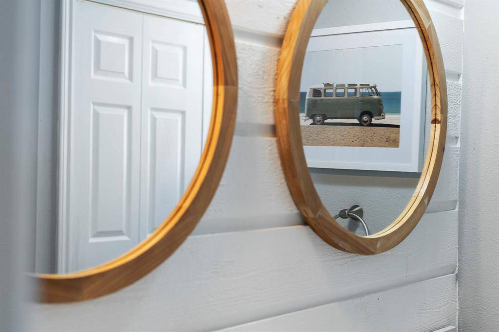 Charming design details include dual wood-framed round mirrors, adding warmth and coastal flair to the bathroom space.