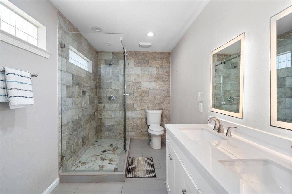 Gorgeous remodeled bath featuring dual vanity with backlit mirrors, modern fixtures, and a spacious walk-in shower with custom tile surround.