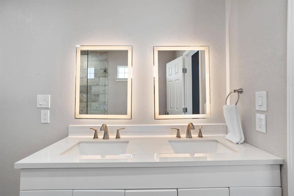 An elegant bath with backlit mirrors, dual vanity, and large walk-in shower with seamless glass enclosure.