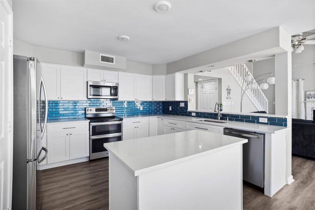 Bright and airy kitchen featuring quartz countertops, large island, stainless appliances, and a stunning ocean-inspired backsplash.